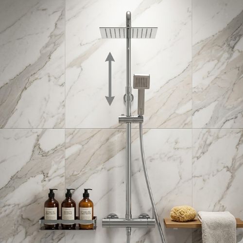 Modern chrome dual-flow rain shower system with a square overhead head and handheld wand, mounted on a luxury white marble wall with spa accessories.