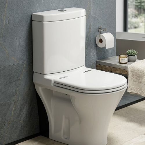 Short-angle view of the Jade WC, a white ceramic toilet with a streamlined design and soft-close lid, set against a grey-veined marble wall in a modern bathroom.