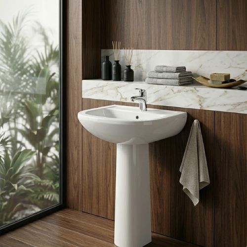 A premium high-gloss white ceramic Alfa washbasin by Neatflow Solution featuring a classic full-pedestal design and a modern polished chrome faucet, set against a luxury dark wood and marble-accented bathroom wall.