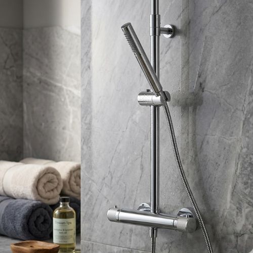 Modern Titan Elite chrome thermostatic shower system mounted on a grey marble wall with spa accessories and plush towels.