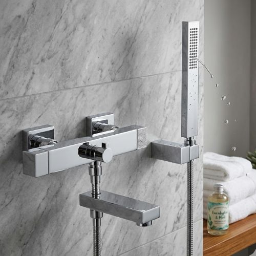 Geometric Cube-Ultima chrome bath and shower mixer with a rectangular handheld wand, mounted on a grey marble wall featuring a waterfall spout and spa accessories.