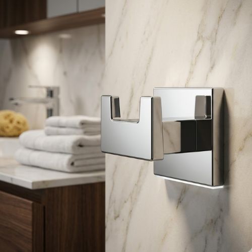 A modern, wall-mounted S-Cube double robe hook in polished chrome, professionally styled against a luxury cream marble wall with a high-end vanity and soft bathroom towels in the background.
