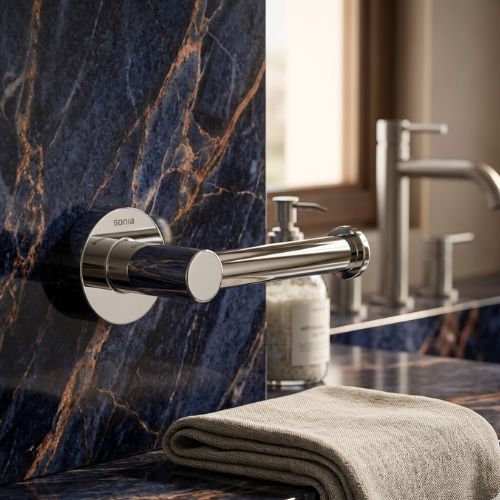 Polished chrome open-arm toilet roll holder mounted on a neutral-toned wall.
