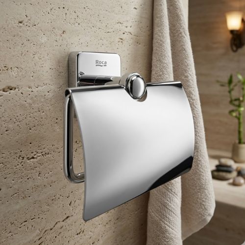 A premium Roca Victoria chrome toilet roll holder with a protective cover, mounted on a luxury stone wall to showcase a clean and hygienic bathroom aesthetic.