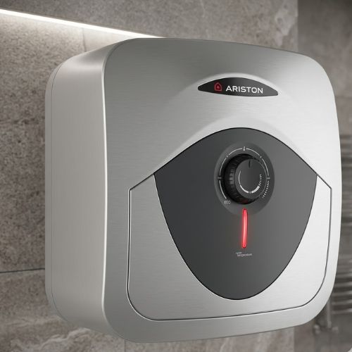 A sleek, wall-mounted Ariston 15L electric water heater with a brushed metallic finish and a glowing red temperature indicator, professionally installed against a modern stone tile bathroom wall.