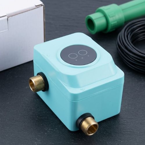An eye-level shot of a modern, compact, automatic AC/DC water booster pump in a sleek cyan casing, professionally installed inline with durable green PPR water pipes against a clean background.