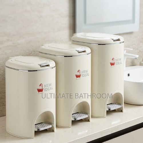 A set of three cream-colored, professional-grade pedal waste bins of varying sizes, arranged neatly on a polished countertop next to a modern bathroom sink.