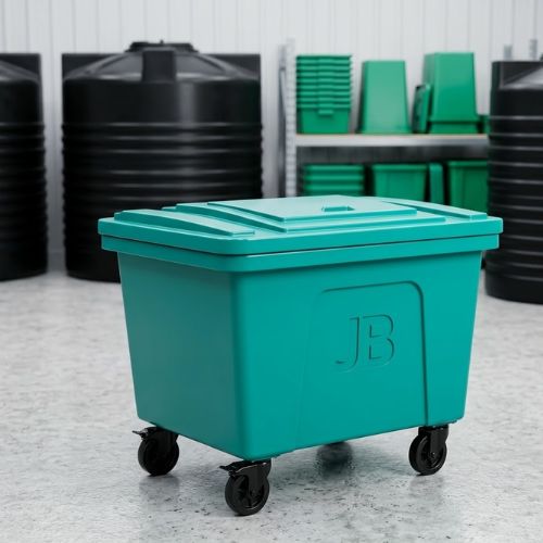A large, teal-colored 1100-litre industrial mobile waste container with a secure lid and heavy-duty wheels, set against the backdrop of a warehouse with storage racking and large water tanks.