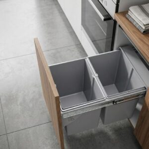 A dual-compartment pull-out waste bin installed inside a wooden kitchen cabinet, featuring a smooth-glide sliding track system.
