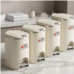 A set of four elegant cream-colored, foot-operated pedal waste bins in varying sizes, arranged on a marble surface.