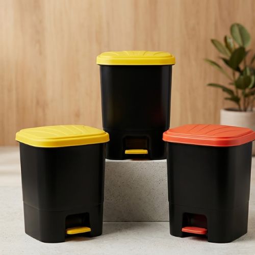 A set of three modern 15-litre black pedal waste bins with yellow and orange lids arranged on a concrete surface.