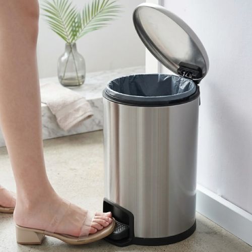 A 3-litre stainless steel pedal bin with a foot-operated lid, shown in a clean, modern bathroom interior with a towel and plant in the background.