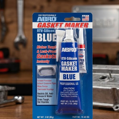A package of ABRO Blue RTV Silicone Gasket Maker, a professional-grade sealant, presented on a workbench with automotive tools in the background.
