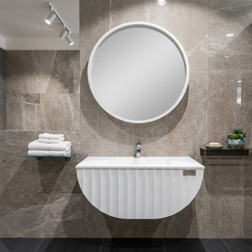 A sleek, modern wall-mounted bathroom vanity with a fluted white finish and a circular mirror in a luxurious, tiled bathroom setting.