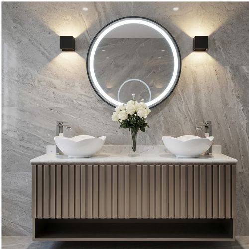 A luxurious floating bathroom double vanity featuring fluted brown cabinetry, two unique wavy-edged vessel sinks, a central bouquet of white roses, and a large, round LED-backlit mirror flanked by modern black sconces against a grey marble wall.