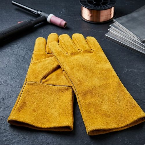 A pair of premium yellow leather welding gloves resting on a dark slate surface next to welding tools and metal plates.